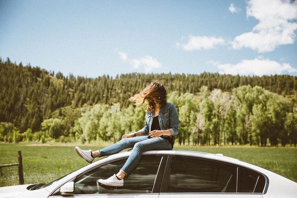 Viajar en el extranjero chica joven subida en un coche con el pelo al viento y detrás montañas